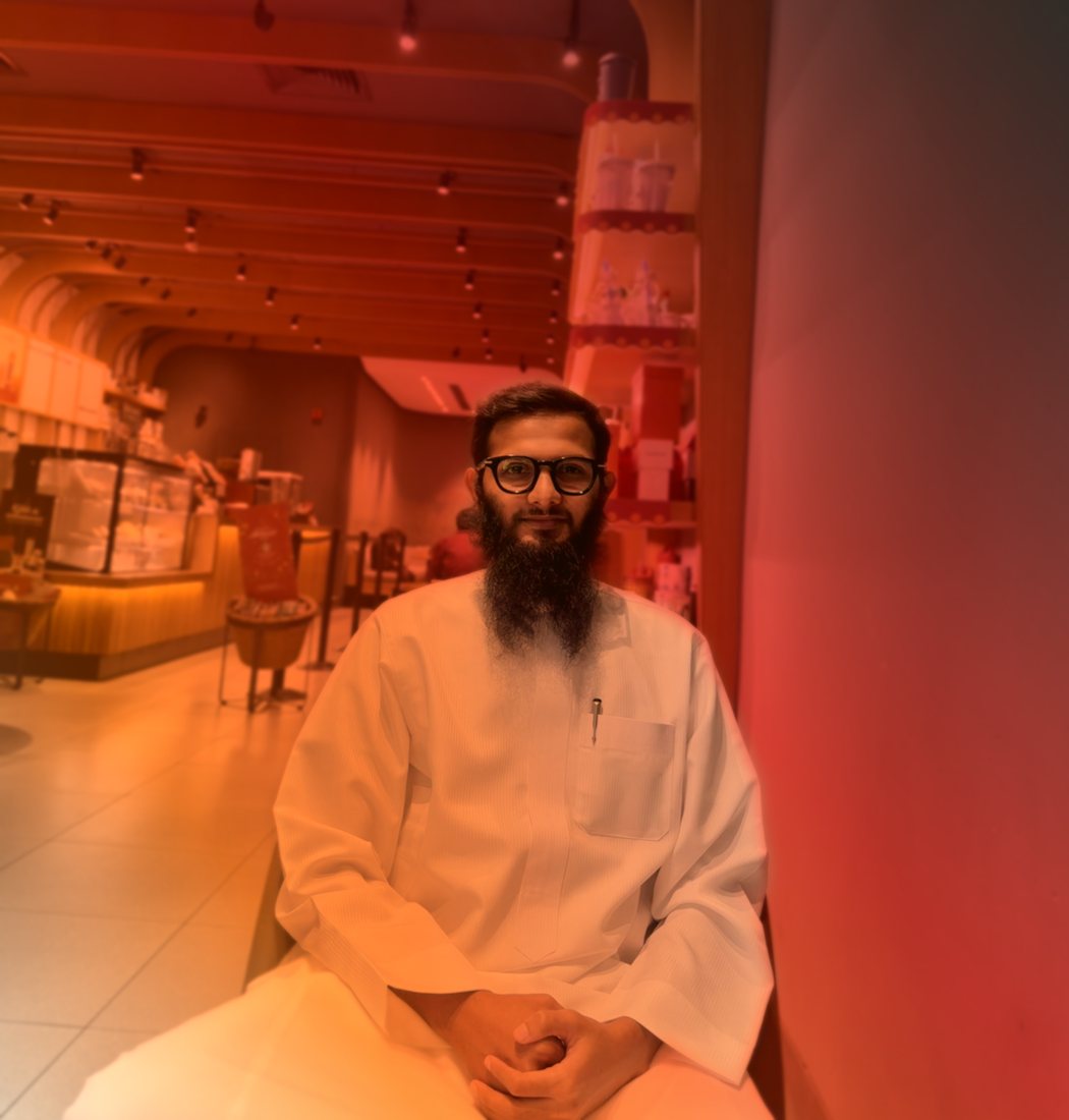Tauseef Ahmed in a white thobe, seated with hands clasped